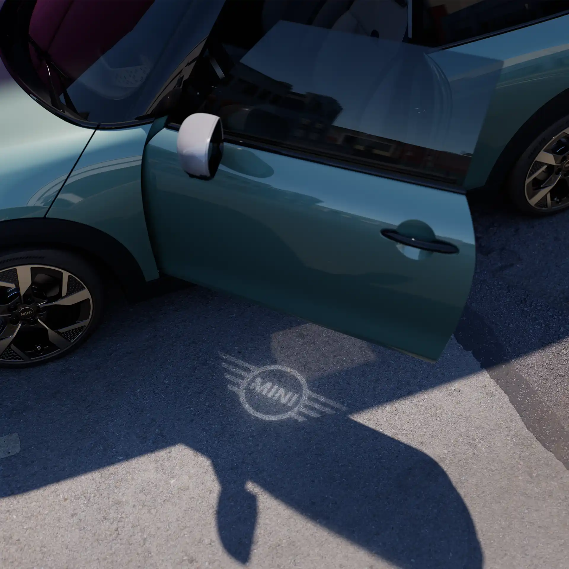 Exterior view of MINI Cooper with open door and MINI logo welcome light on the ground 