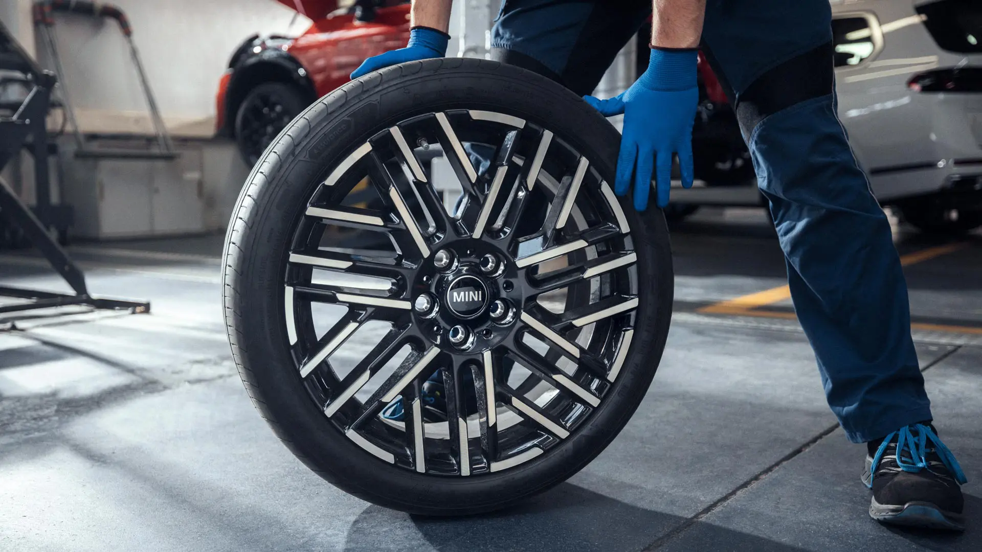 A MINI Partner service technician rolls an 18" Night Flash Spoke Bicolour Light Alloy Wheel into position.